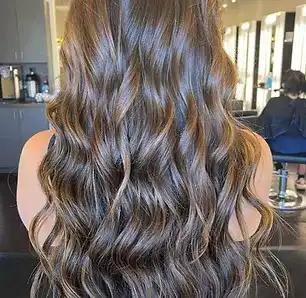 Woman with long, wavy brown hair sitting in a salon.