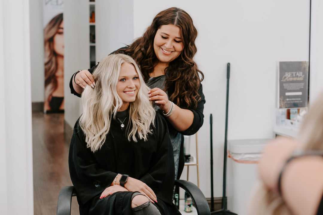 Hairstylist working on a smiling client's hair in a modern salon.