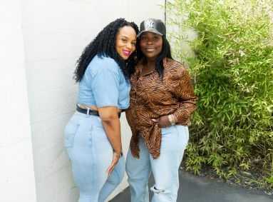 Two women smiling and posing together in casual outfits outdoors near a bamboo plant.